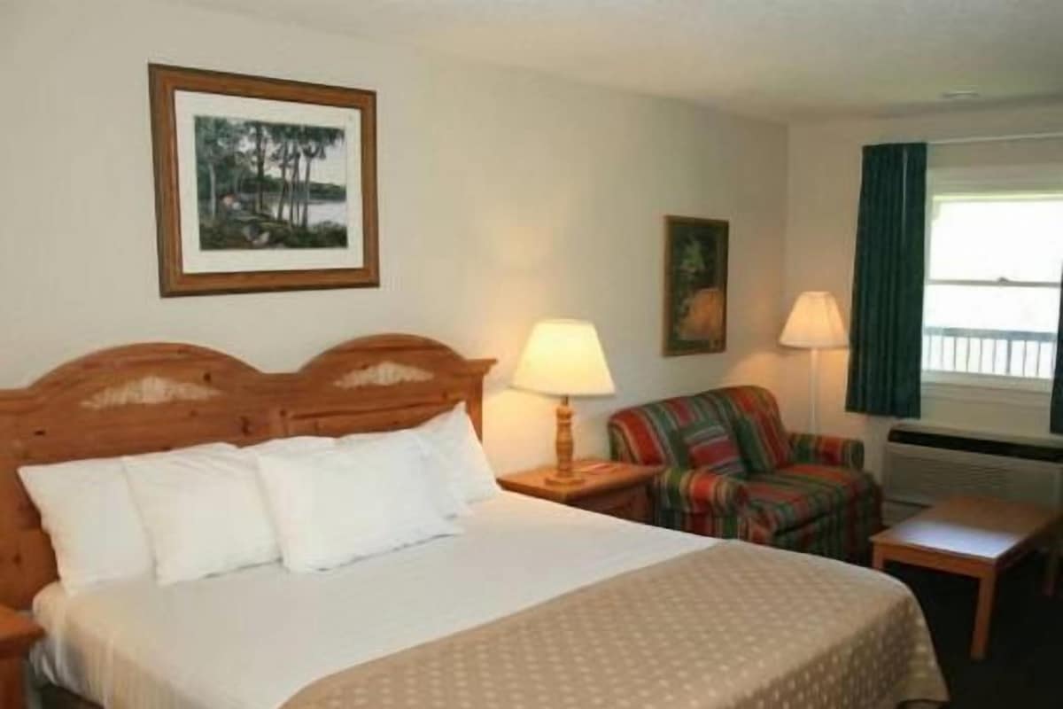 A hotel room with a bed, a chair, a table, and a window with curtains.