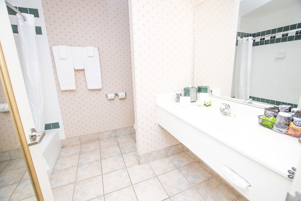 Un baño con ducha, inodoro, lavamanos con artículos de aseo y un espejo.