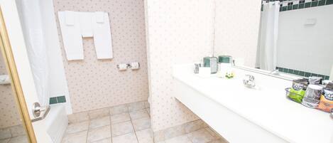Een badkamer met een douche, toilet, wastafel met toiletartikelen en een spiegel.