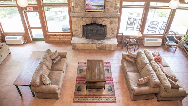 A spacious living area with a stone fireplace, two sofas, a wooden coffee table, and a view through large windows. - Lake Chatuge Lodge (Hiawassee)