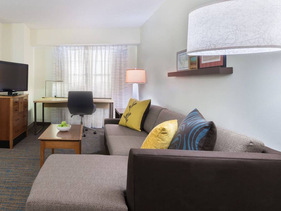 Quarto de hotel com sofá, escrivaninha, televisão e abajur.