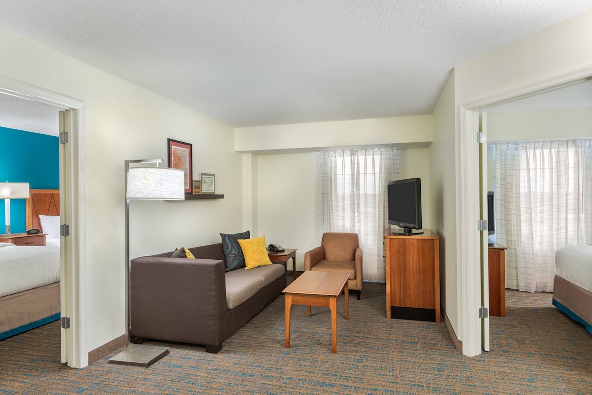 A hotel room with a bed, a sofa, a chair, a TV, and a small table.