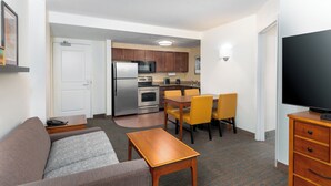 Een gezellig, ruimtelijk ingerichte leefruimte met kitchenette, een bank, een eettafel met stoelen en een televisie op een dressoir.