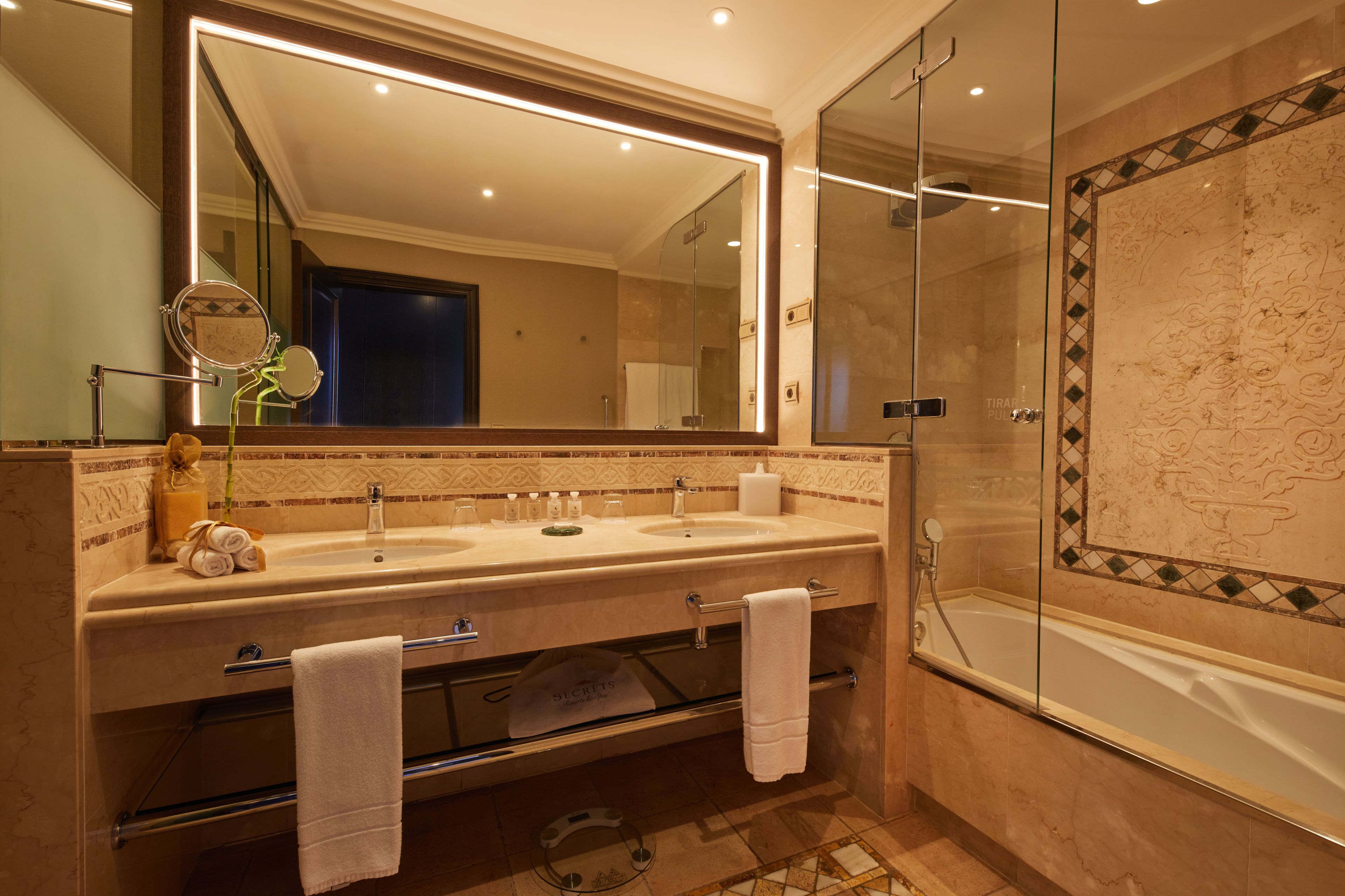A bathroom with a double sink, a large mirror, a glass shower enclosure, and a tiled floor.