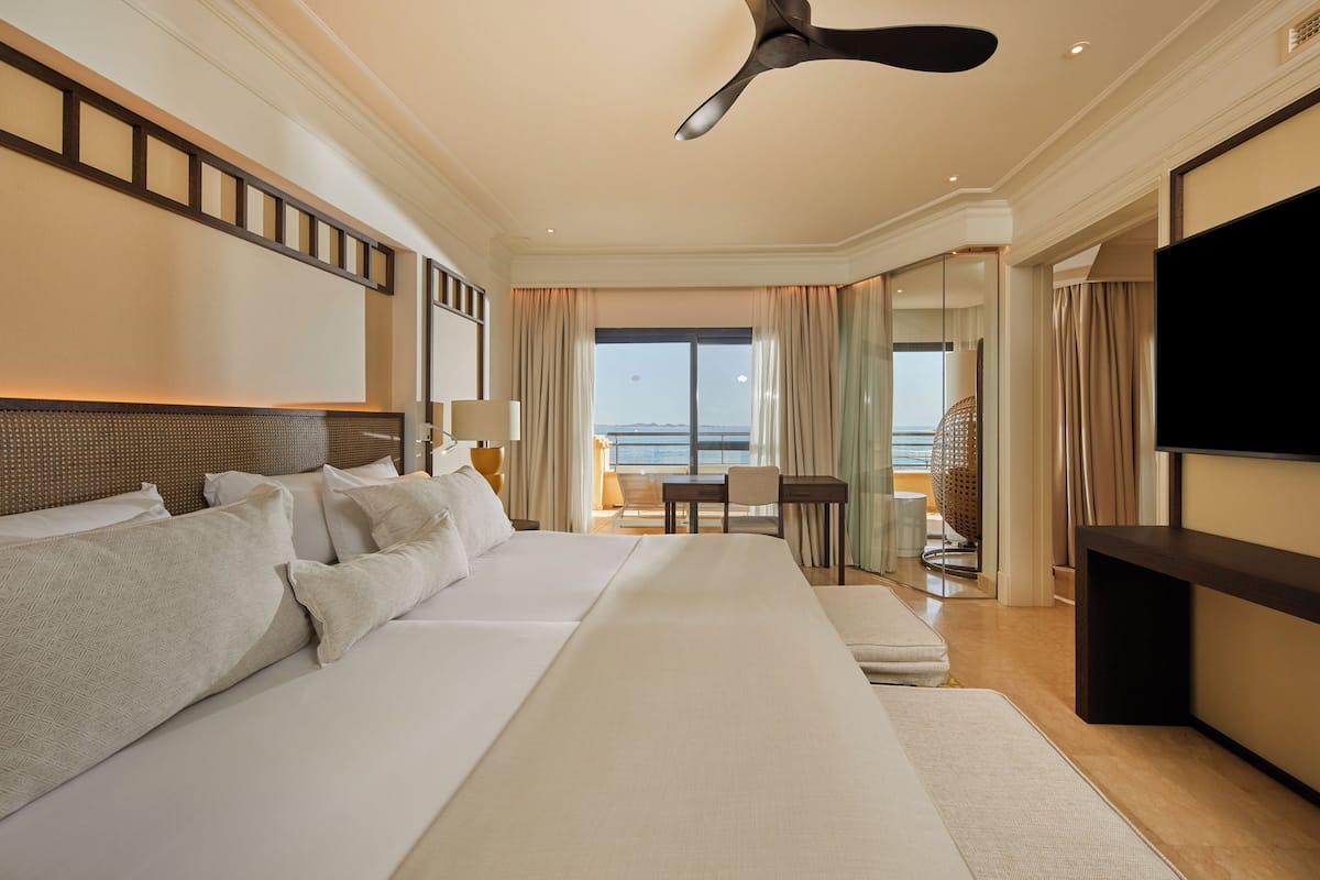 Ein geräumiges Hotelzimmer mit einem großen Bett, einem Flachbildfernseher, einem Deckenventilator und einem Balkon mit Meerblick.