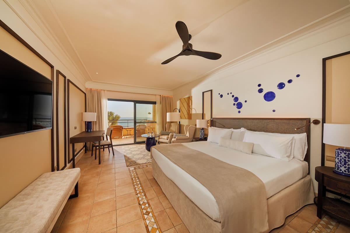 Ein Hotelzimmer mit einem großen Bett, einem Deckenventilator, einem Fernseher, einem Balkon mit Blick und einer Essecke mit Tisch und Stühlen.