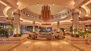 A spacious lobby with a central seating area, large columns, and a modern chandelier.