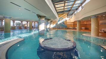 Uma piscina interior com hidromassagem, colunas revestidas de azulejos e teto de vidro.