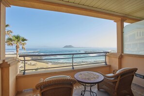 Un balcón con mobiliario de mimbre, vista a la playa y una montaña distante.
