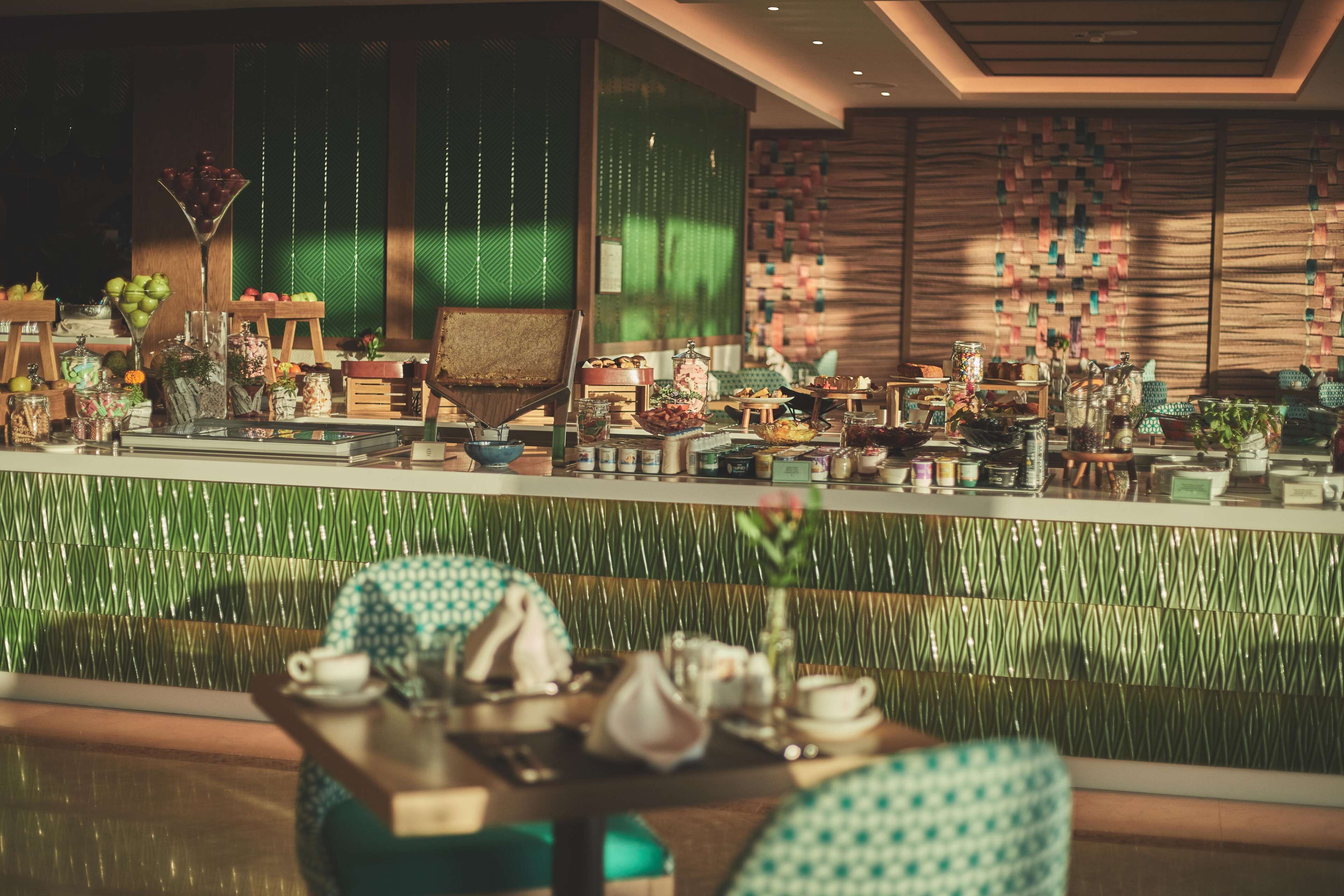 A restaurant with a green-tiled wall, wooden furniture, and various food and drink items on display.