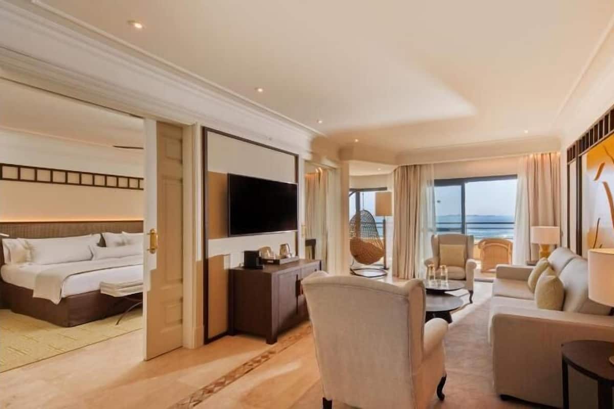 Ein Hotelzimmer mit Bett, Fernseher, Sitzecke inklusive Sofa und Sesseln sowie Meerblick.