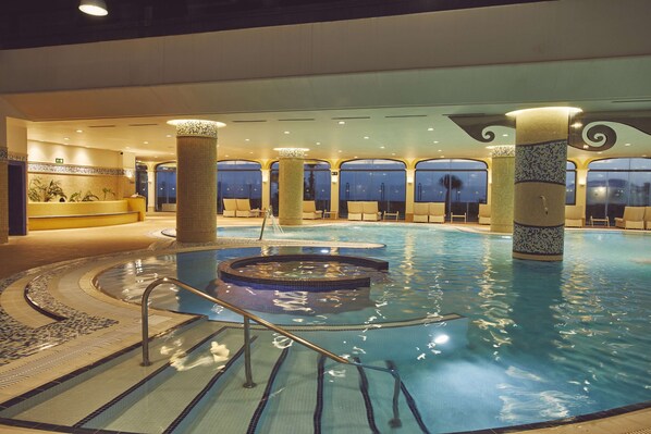Une piscine intérieure dotée d’un jacuzzi, d’escaliers carrelés et de colonnes.
