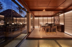 Un comedor moderno con techo de madera, paredes de vidrio y vista a una palmera.