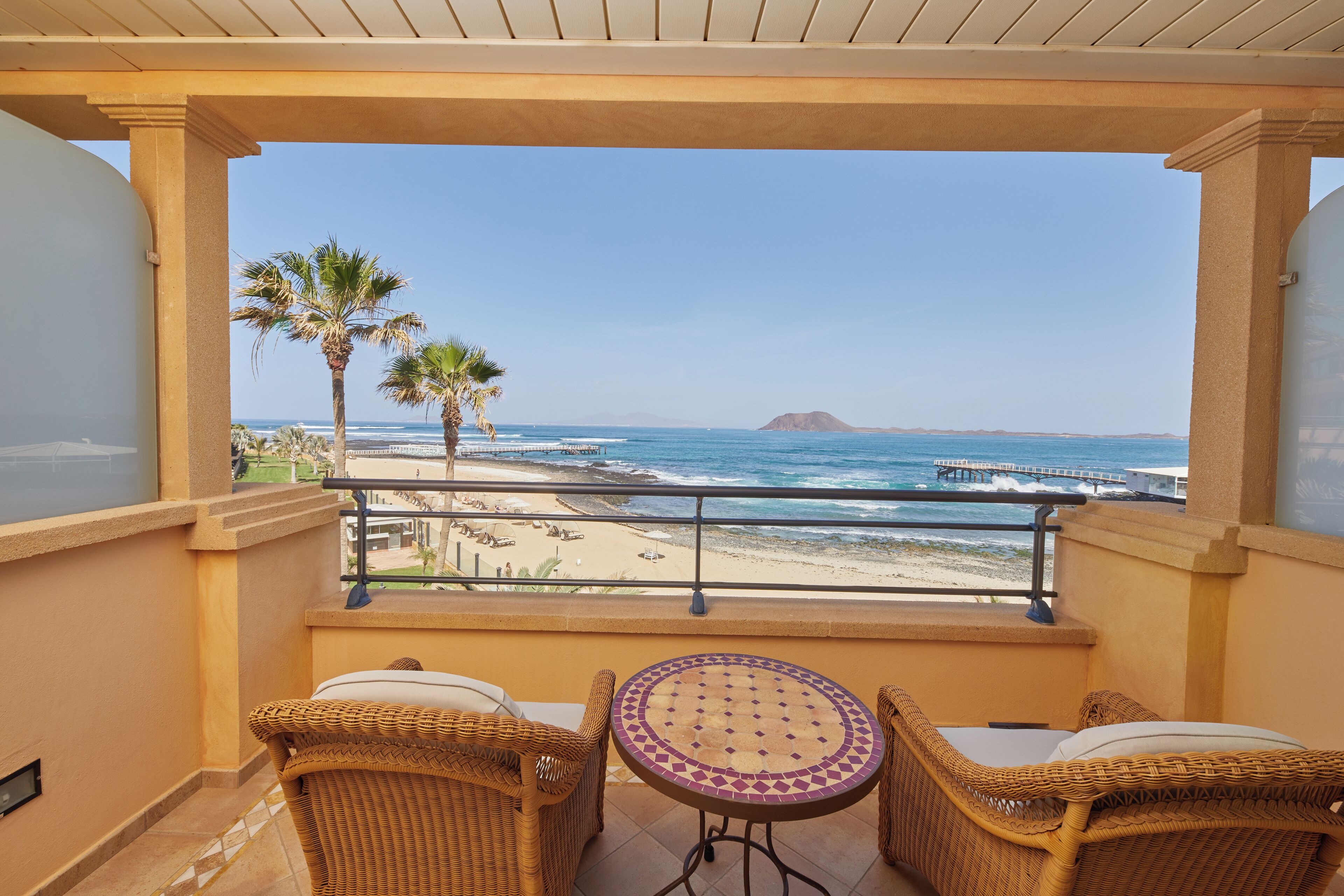 Un balcon doté de meubles en osier et offrant une vue sur la plage et l’océan.