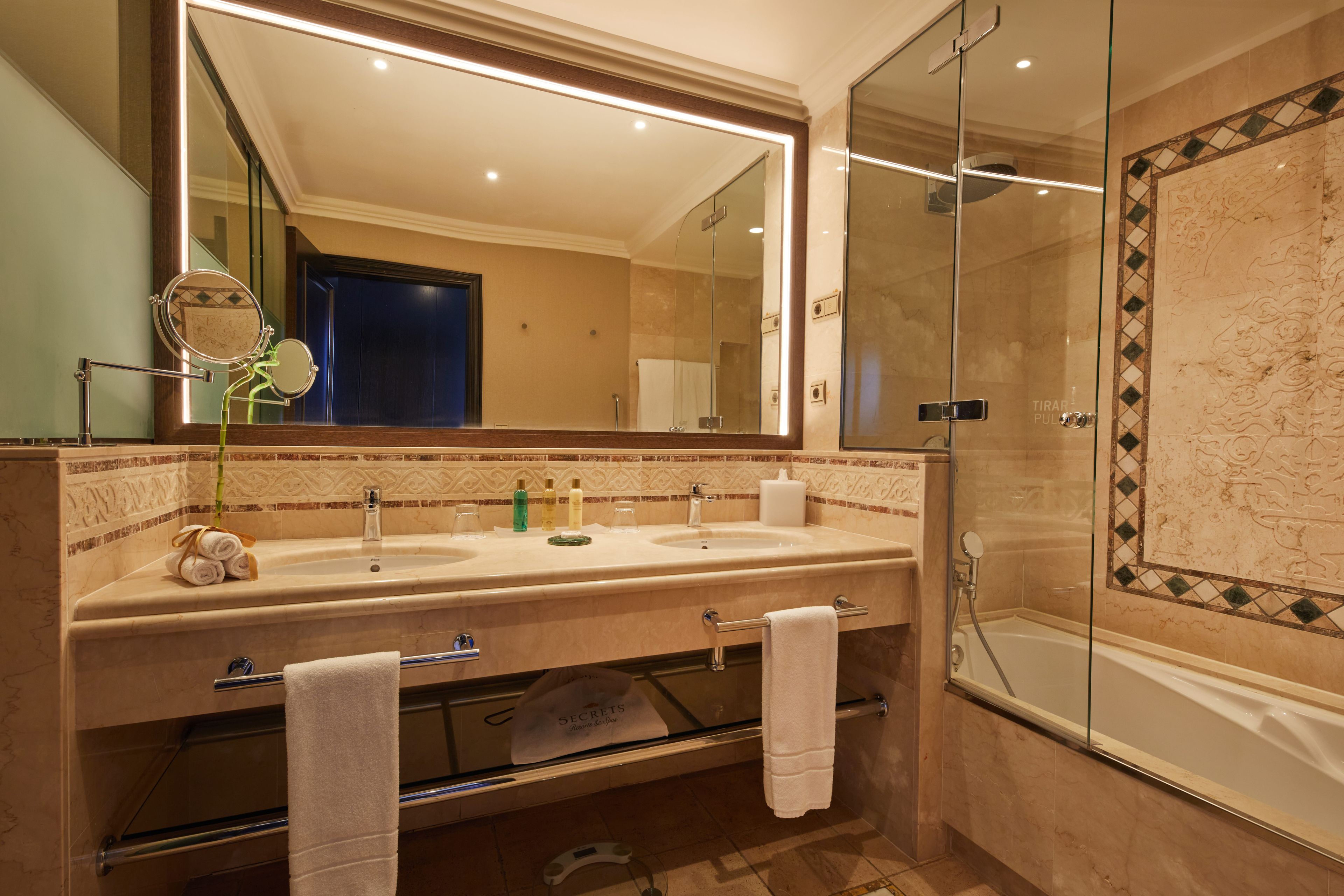 Un baño con un espejo grande, dos lavamanos, una cabina de ducha de vidrio y un perchero para toallas.