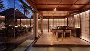 A modern indoor dining area with a wooden ceiling, glass walls, and a seating arrangement.