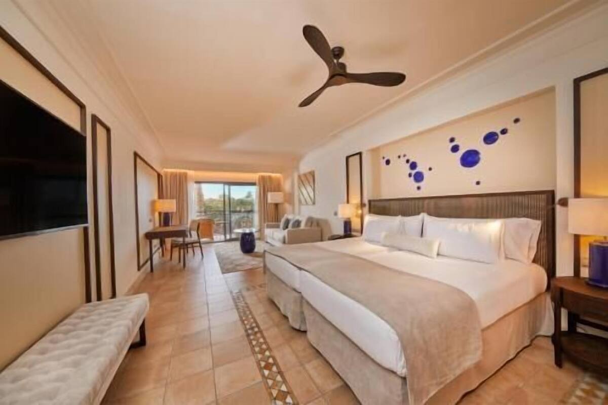 Ein Hotelzimmer mit einem großen Bett, einem Schreibtisch, einem Stuhl und einem Deckenventilator.