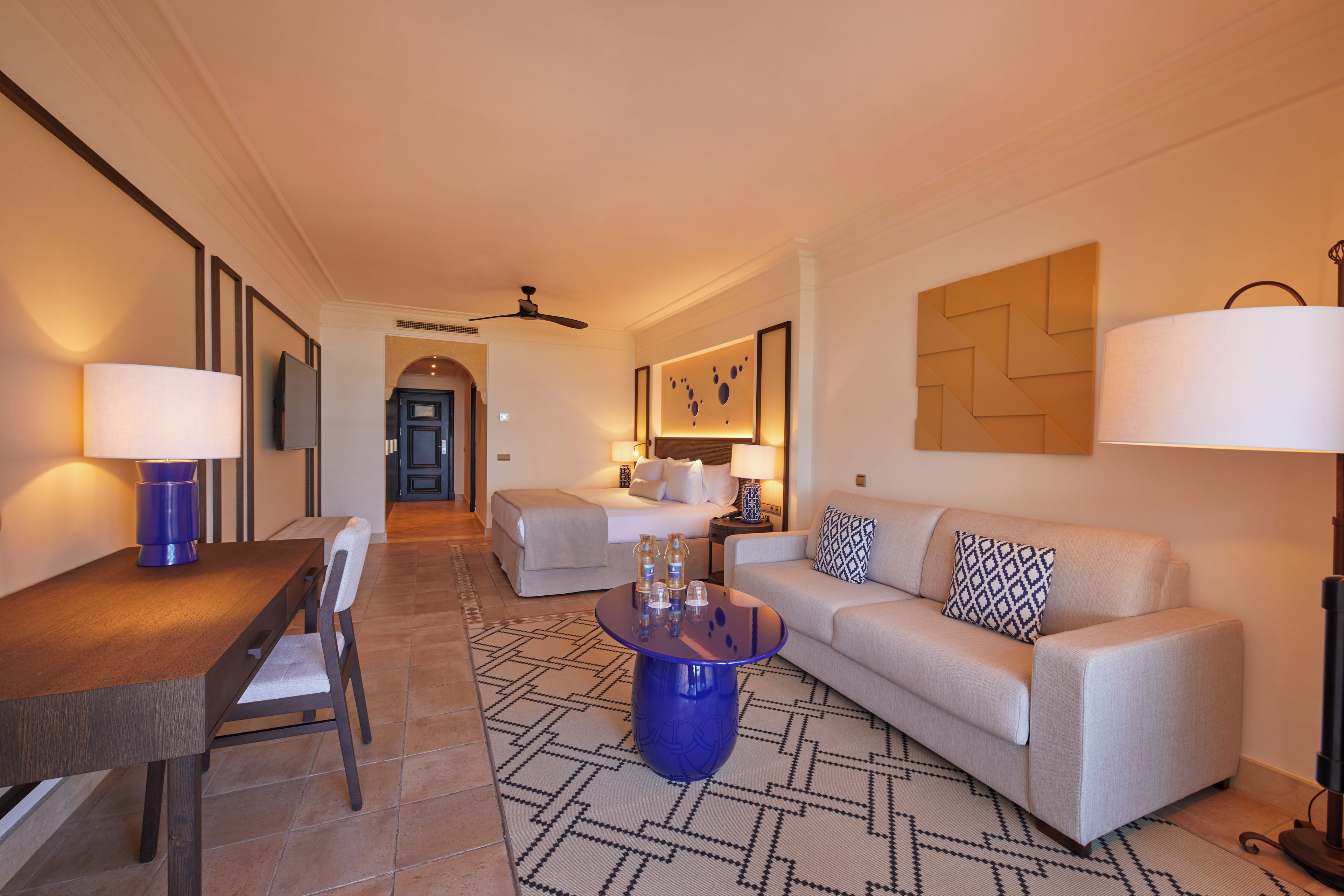 Una habitación de hotel con una mesa de comedor, un sofá, una mesa baja y un televisor.
