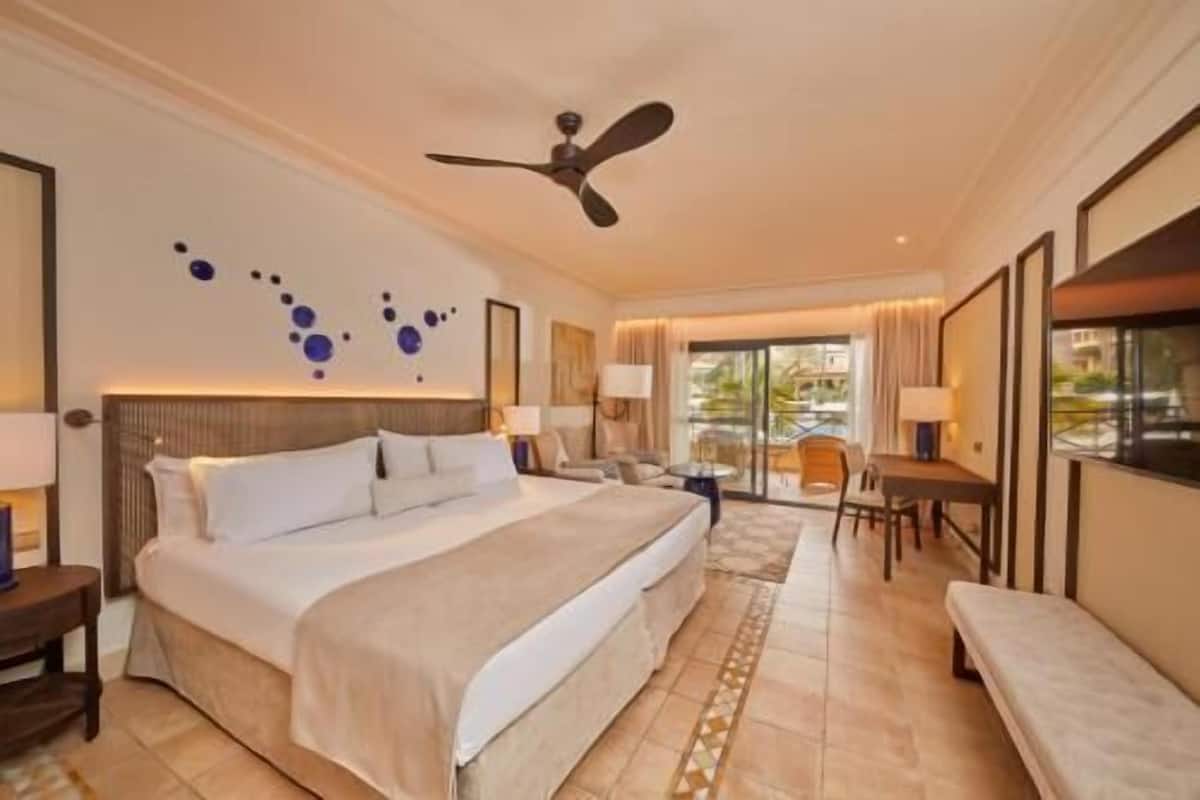 Ein Hotelzimmer mit einem großen Bett, einem Schreibtisch, einem Stuhl, einem Deckenventilator und Blick ins Freie.