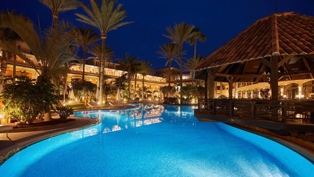 A swimming pool surrounded by palm trees and a building with a tiled roof.
