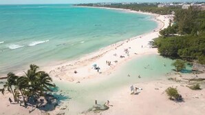 Una playa con agua turquesa cristalina, palmeras y gente disfrutando la arena.