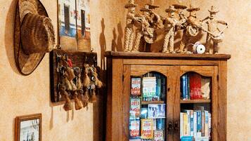 Una habitación con un aparador de madera lleno de libros y revistas, un sombrero colgado en la pared y una pequeña estantería con figuritas.