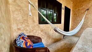 Una hamaca atada a una pared, una maleta con un cojín de colores y una ventana con un letrero.