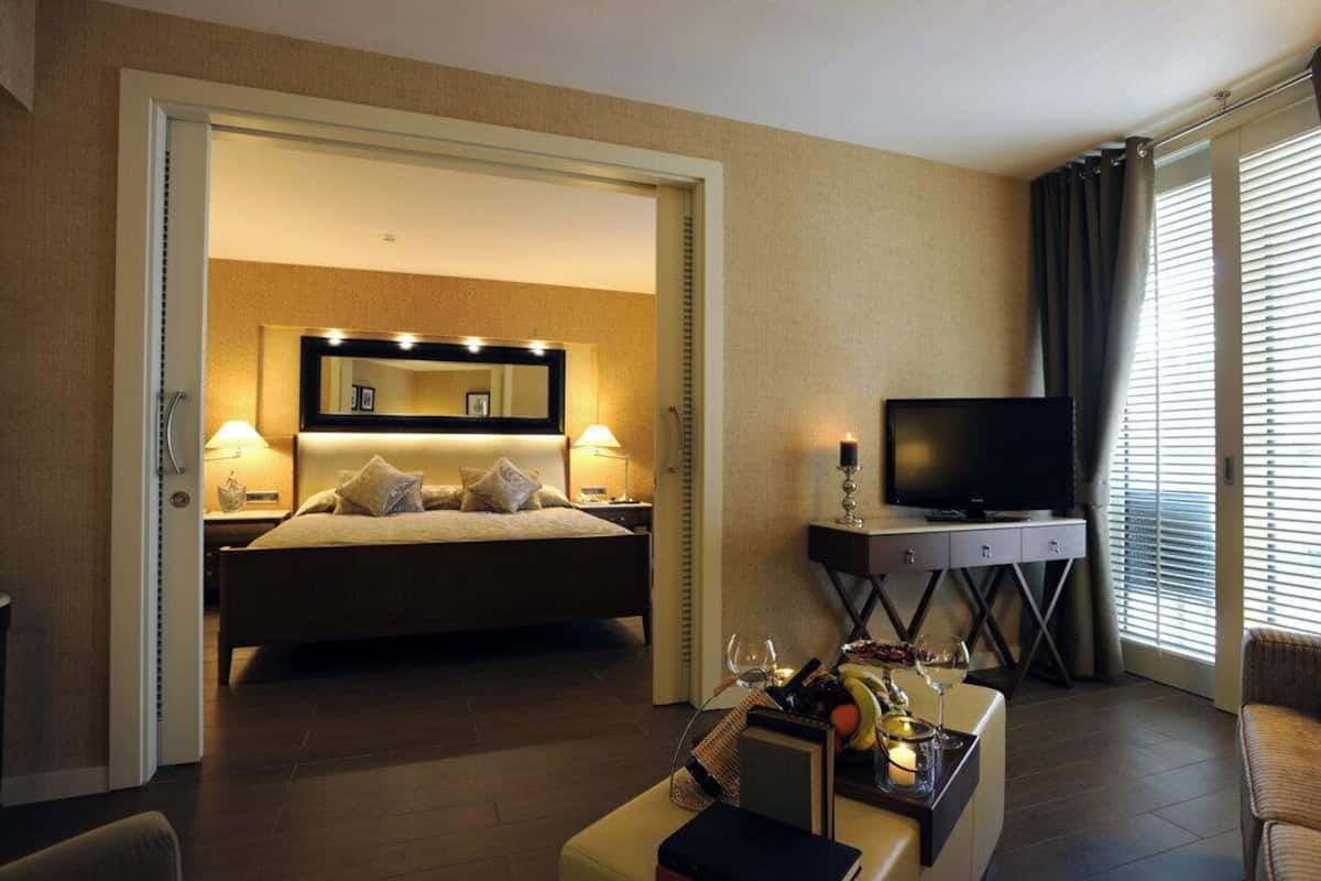 A hotel room with a bed, a TV, a desk with a lamp, and a window with curtains.