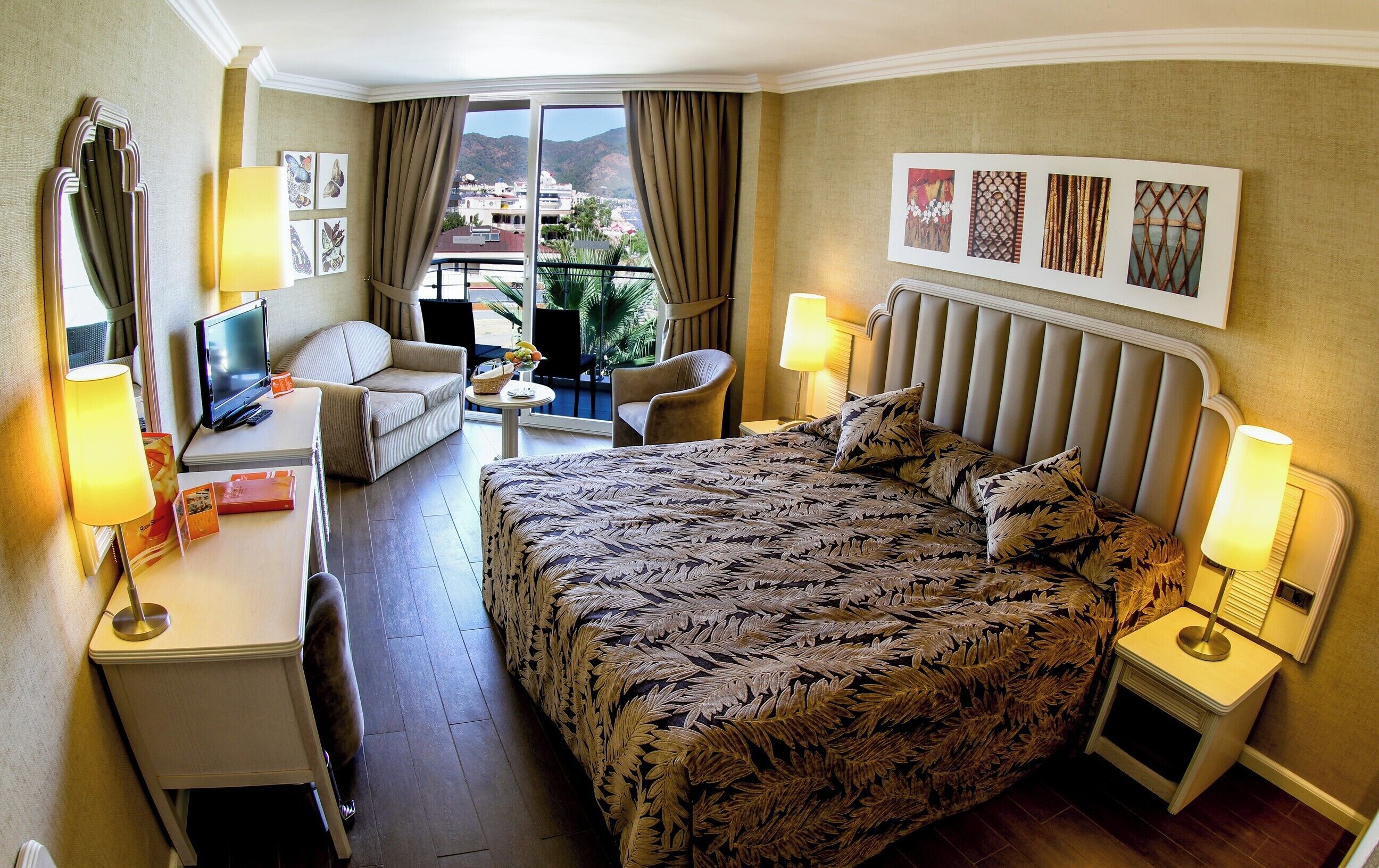 Een hotelkamer met een bed, een bureau, een stoel, een klein tafeltje en een balkon met uitzicht.