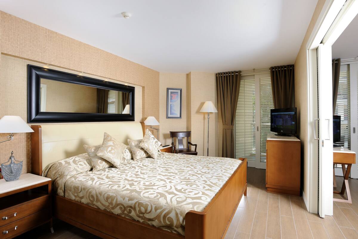 A hotel room with a large bed, bedside lamps, a flat-screen TV, a mirror, and a door leading to a balcony.
