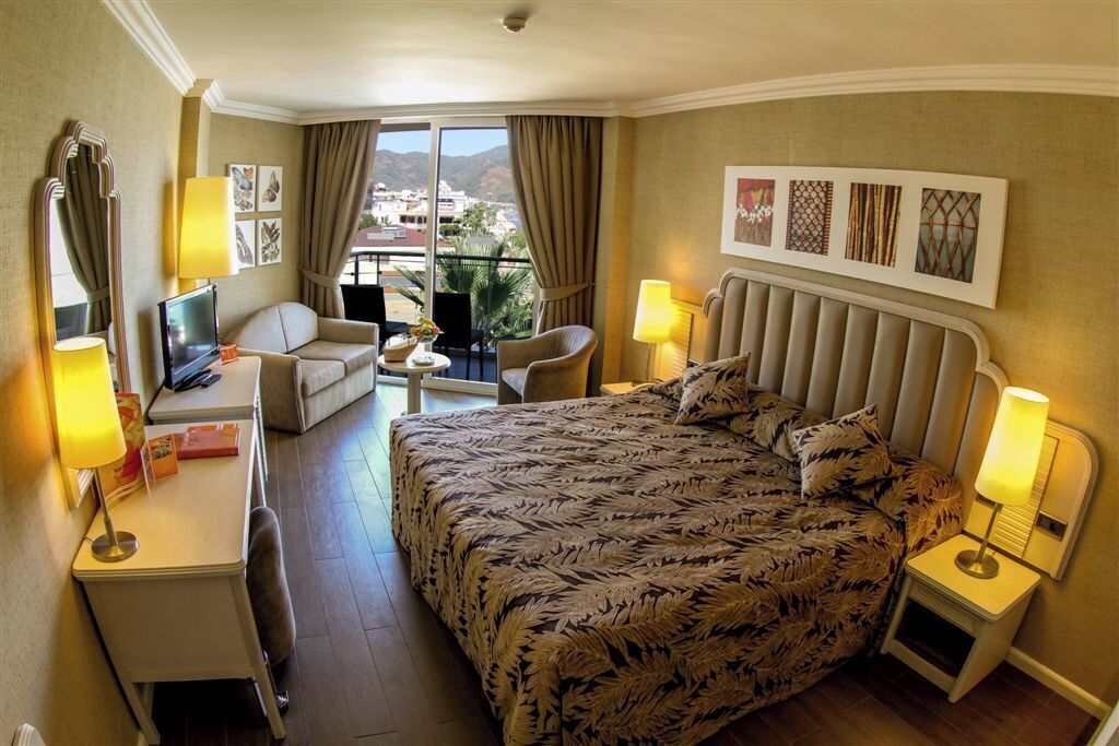 Een hotelkamer met een bed, een bureau, een stoel, een televisie en een balkon met uitzicht.