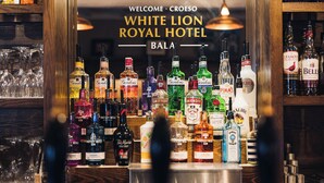 A bar with a variety of liquor bottles and glasses. - White Lion Royal Hotel (Bala)