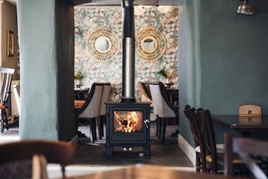 Una habitación acogedora con estufa de leña, papel tapiz estampado y un comedor con sillas y mesa.