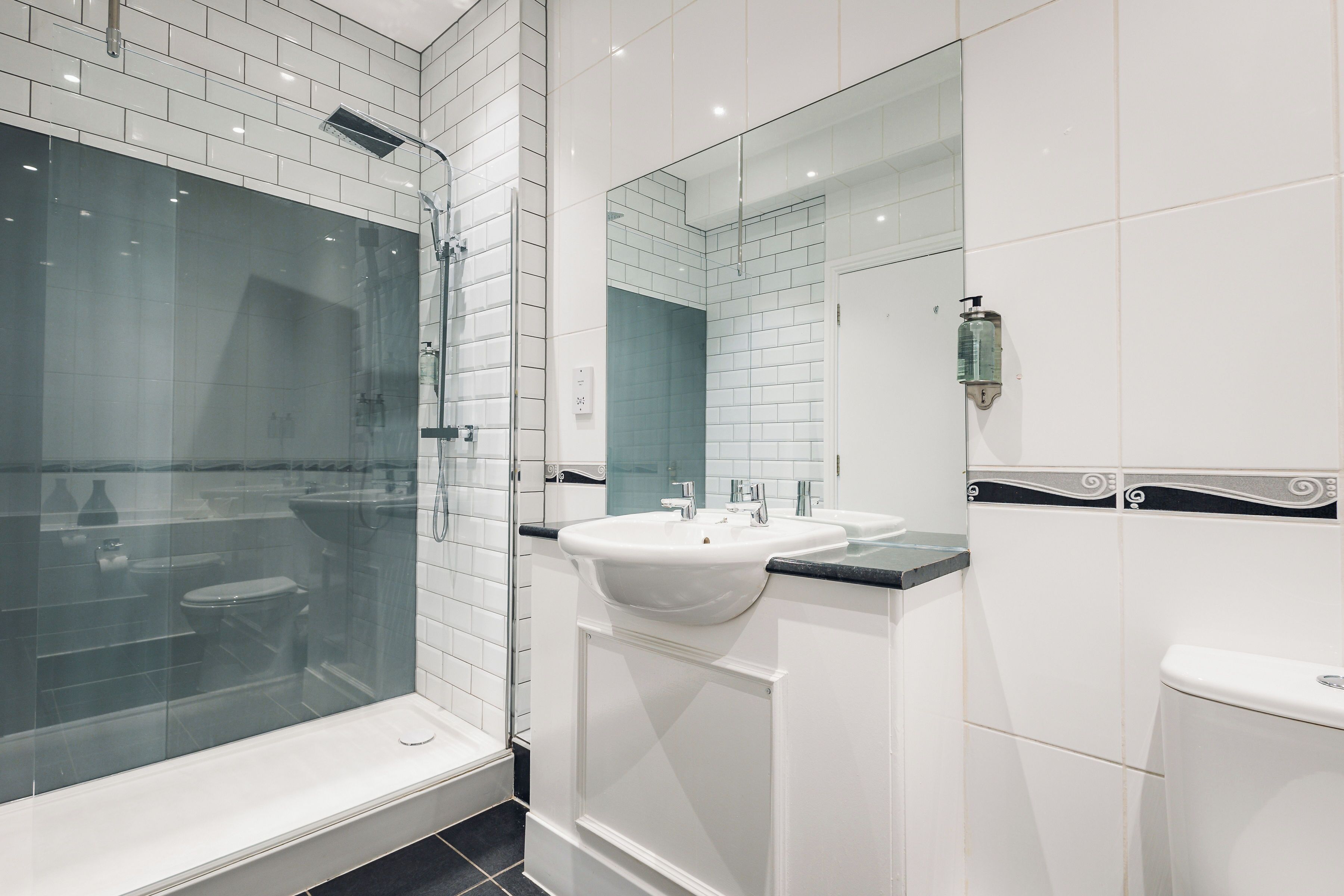 A modern bathroom with a glass-enclosed shower, a white sink, and a large mirror.