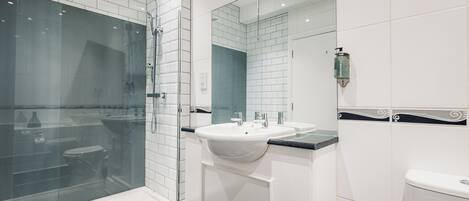 Un baño moderno con ducha de vidrio, lavamanos blanco y un espejo grande.