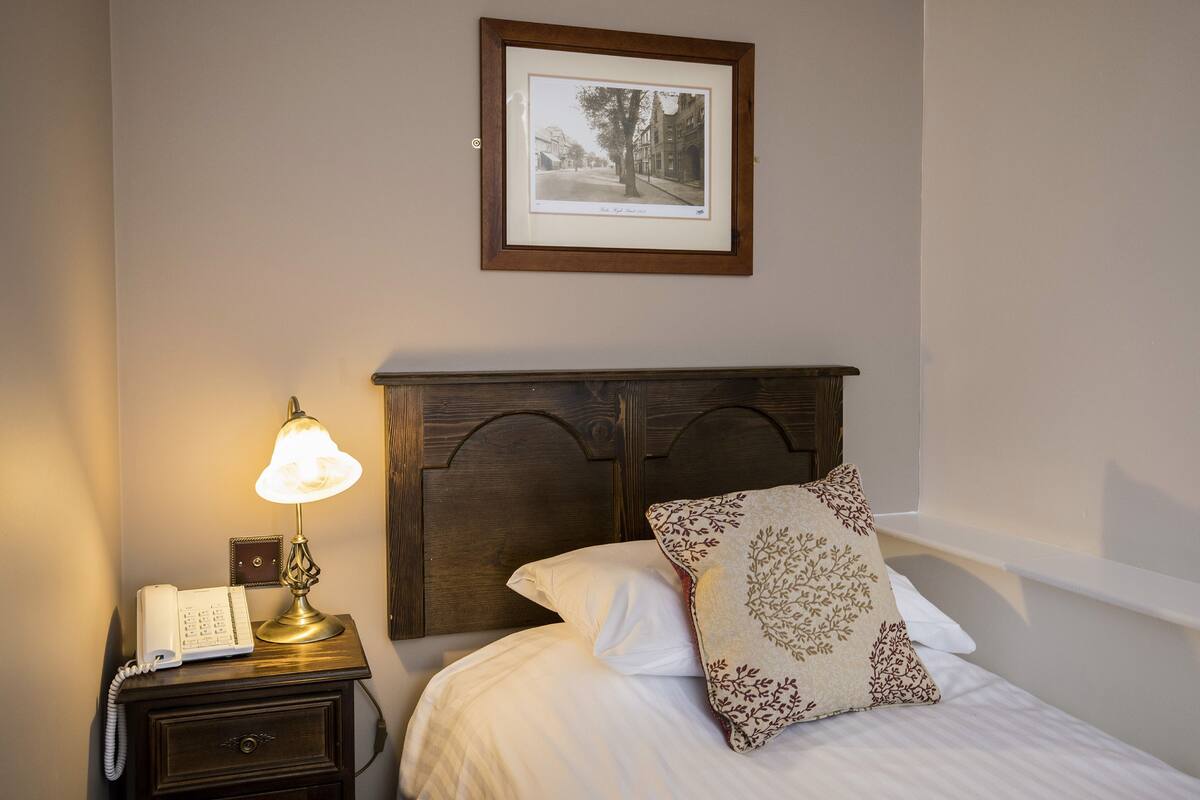 Un lit bien fait, agrémenté d’un coussin décoratif, d’une lampe de chevet et d’un tableau encadré accroché au mur au-dessus.