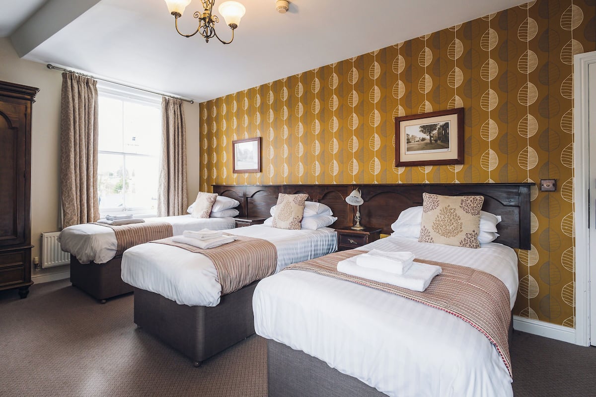Une chambre d’hôtel avec deux lits, une grande fenêtre et un papier peint à motifs.