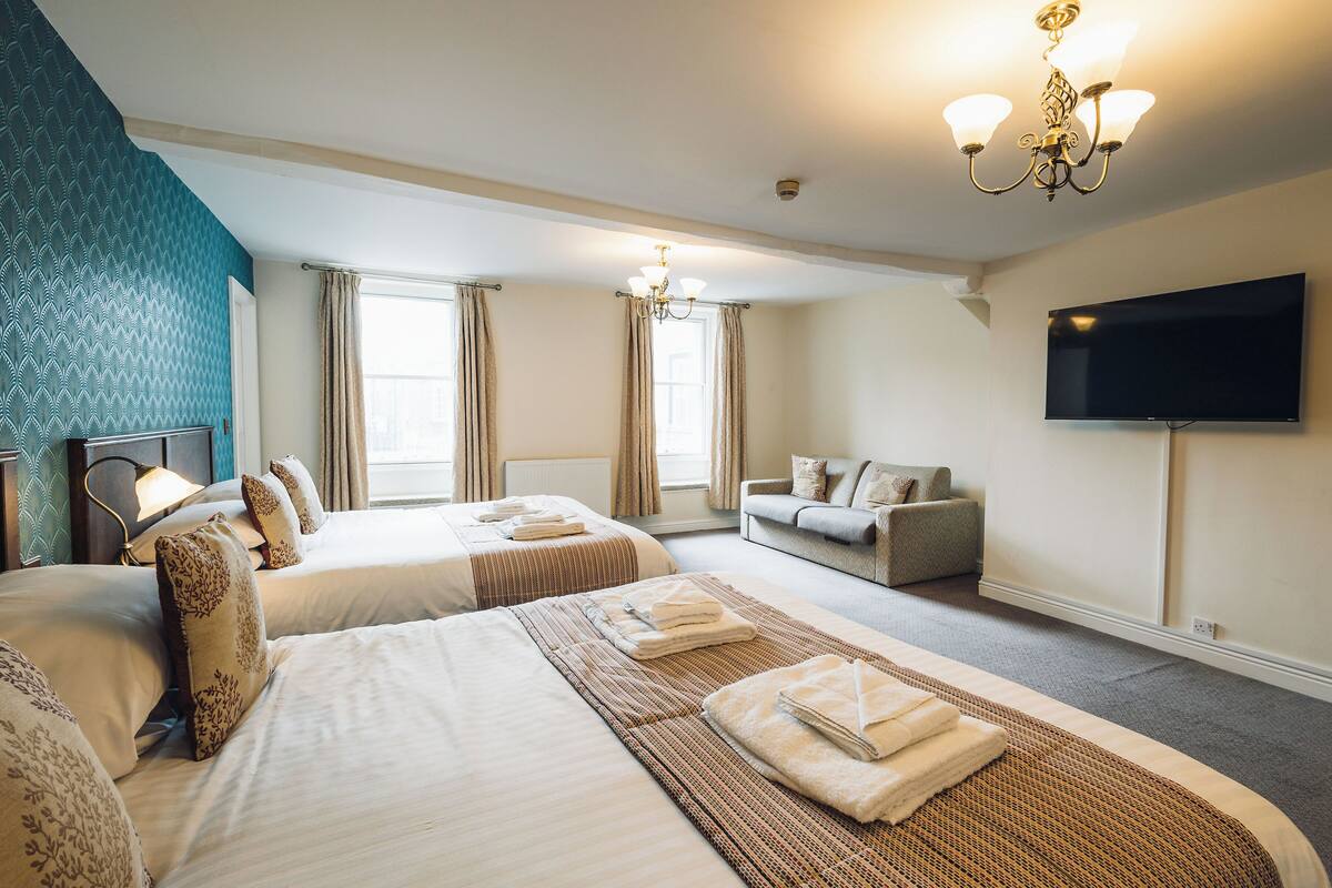 Une chambre d’hôtel avec deux lits, un canapé, une télévision et un lustre.
