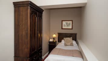 Un dormitorio con un armario de madera grande, una mesita de noche con lámpara y un cuadro enmarcado en la pared.