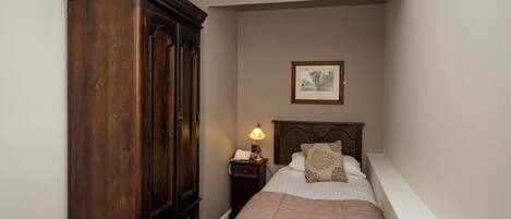 Una camera da letto con un'ampia armadiatura in legno, un comodino con una lampada e un quadro appeso alla parete.