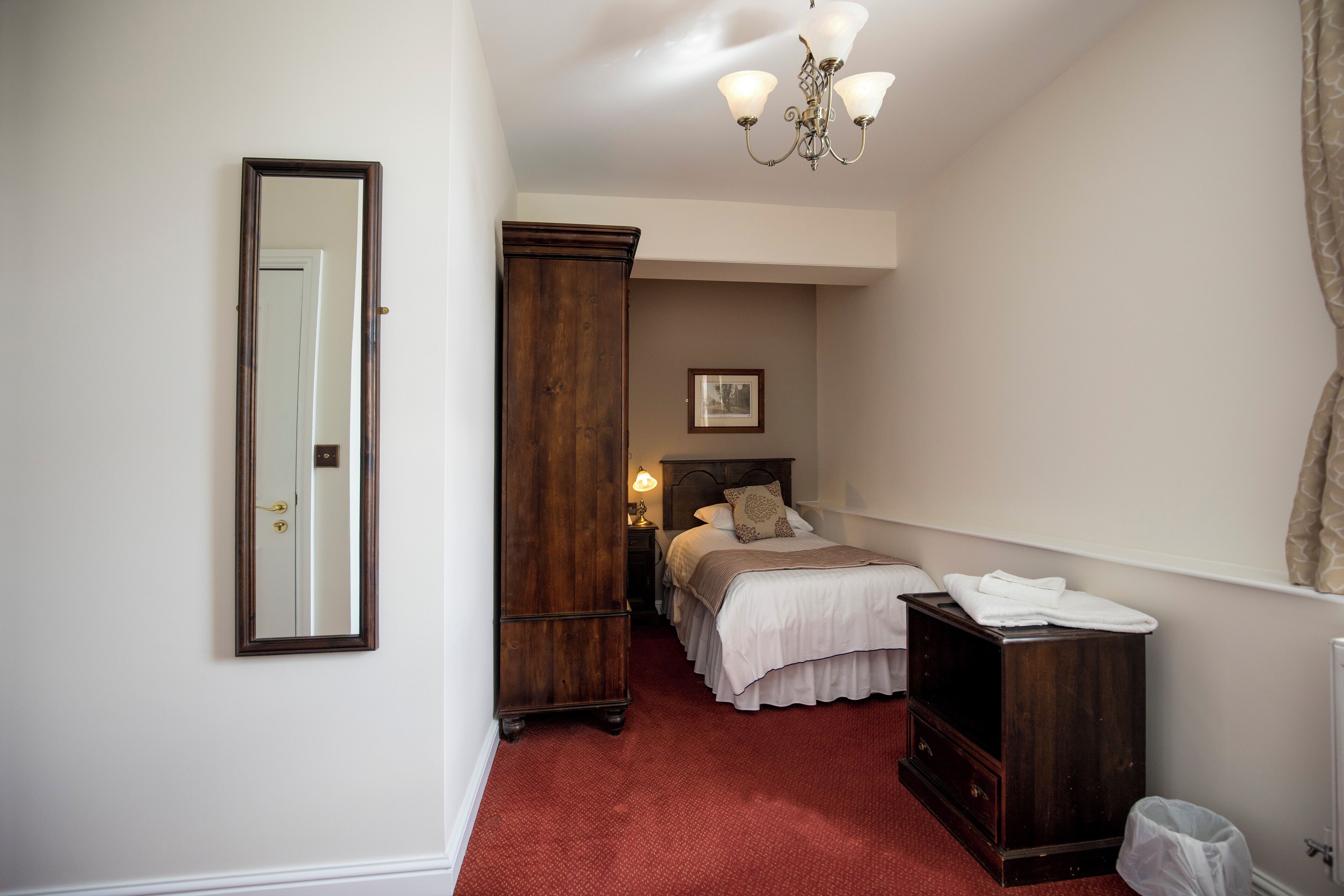 A bedroom with a bed, a wardrobe, a mirror, a chandelier, and a radiator.