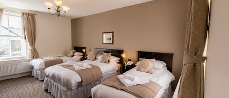 Habitación de hotel con tres camas, un candelabro, un cuadro enmarcado en la pared y una ventana con cortinas.