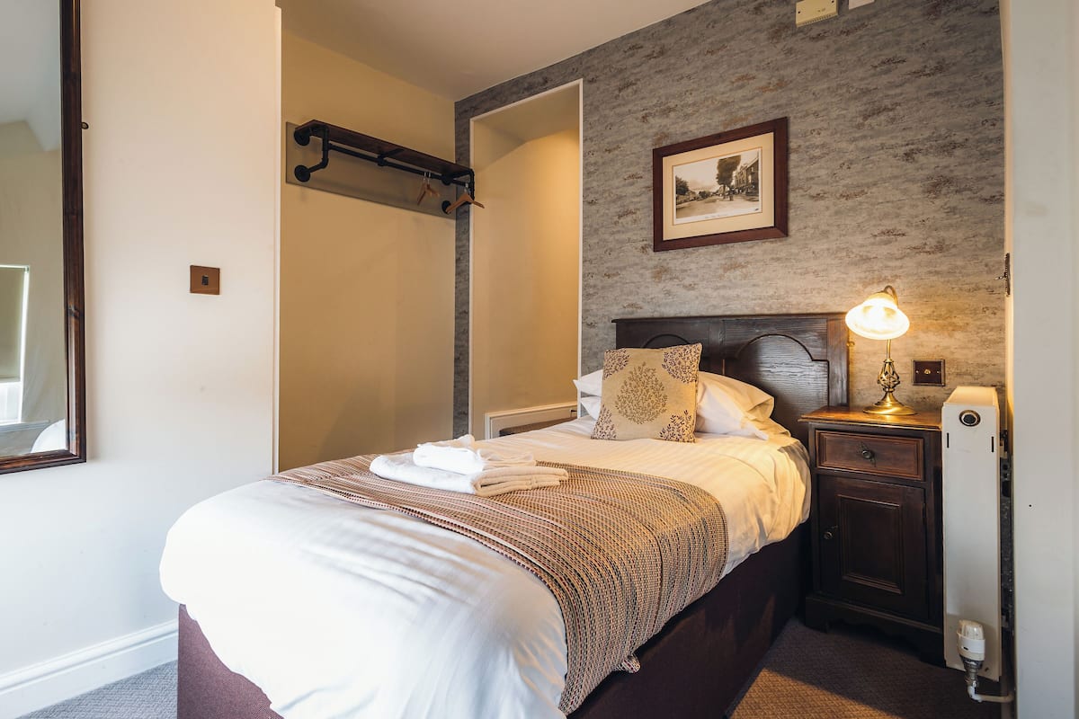 Un lit bien fait, avec une couverture à motifs, une lampe de chevet et un tableau encadré accroché au mur.