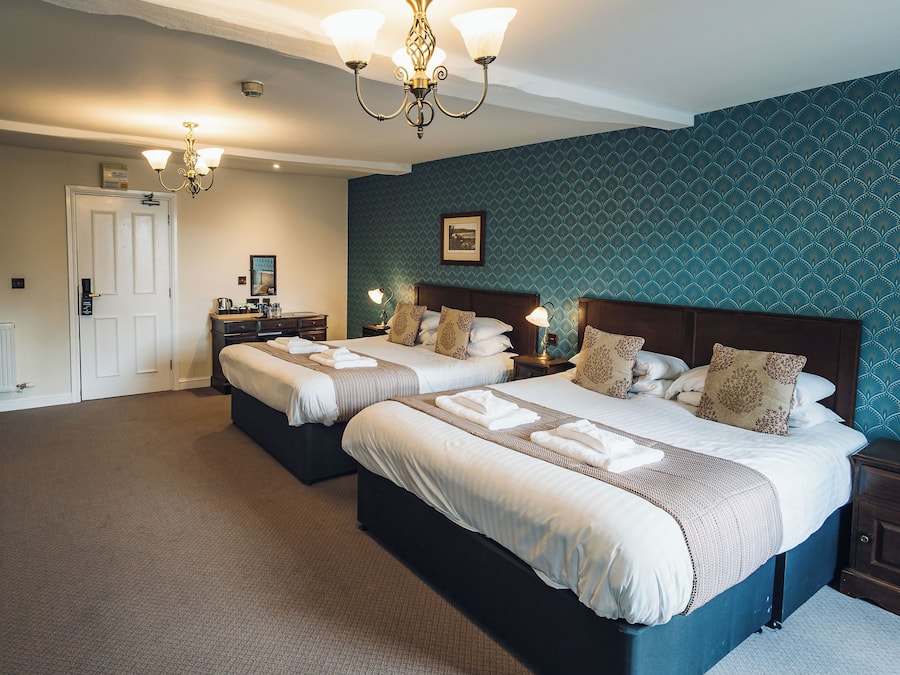 A hotel room with two beds, a chandelier, a blue patterned wall, and a white door.