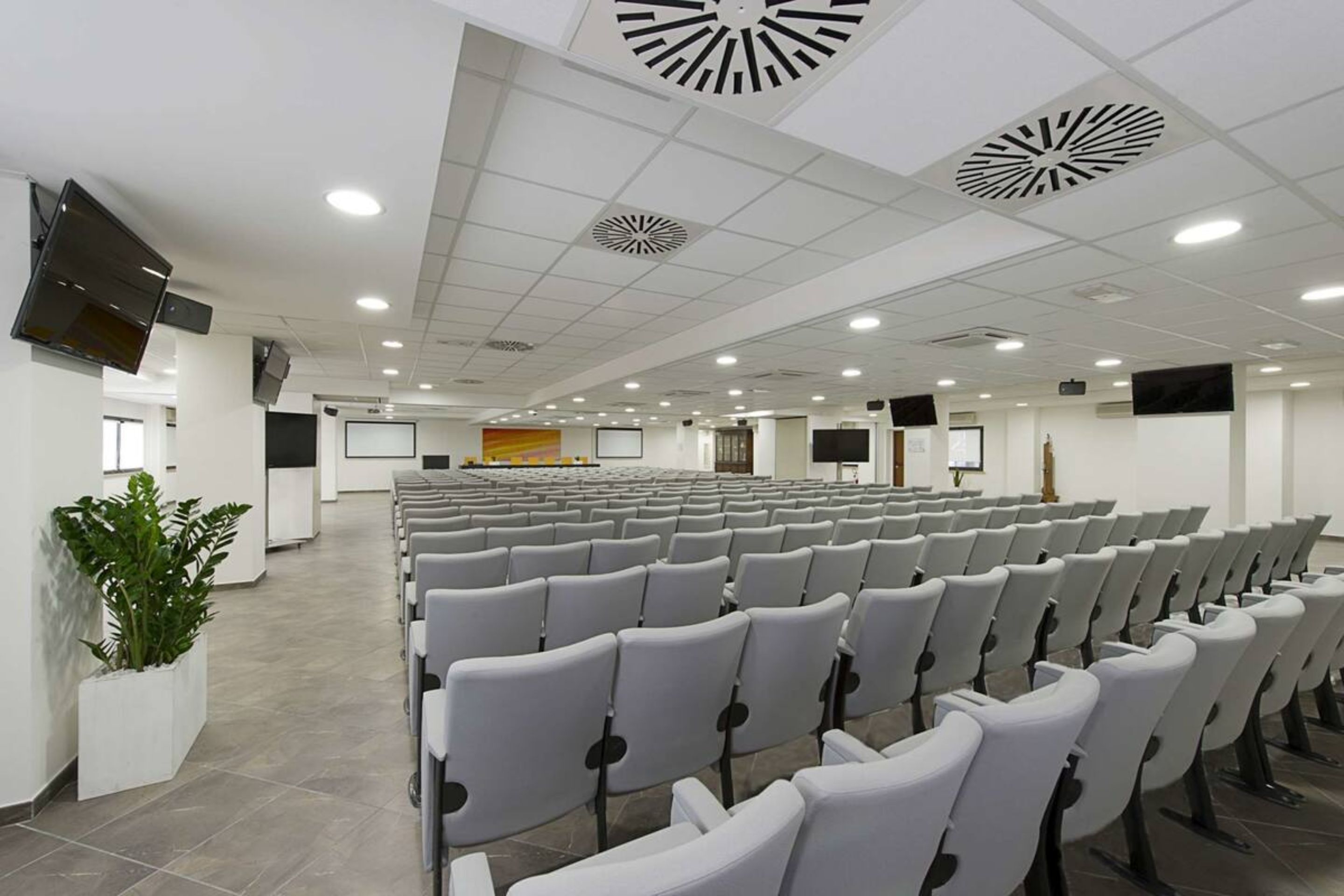 Une salle de conférence avec des rangées de chaises, une scène et un grand écran.