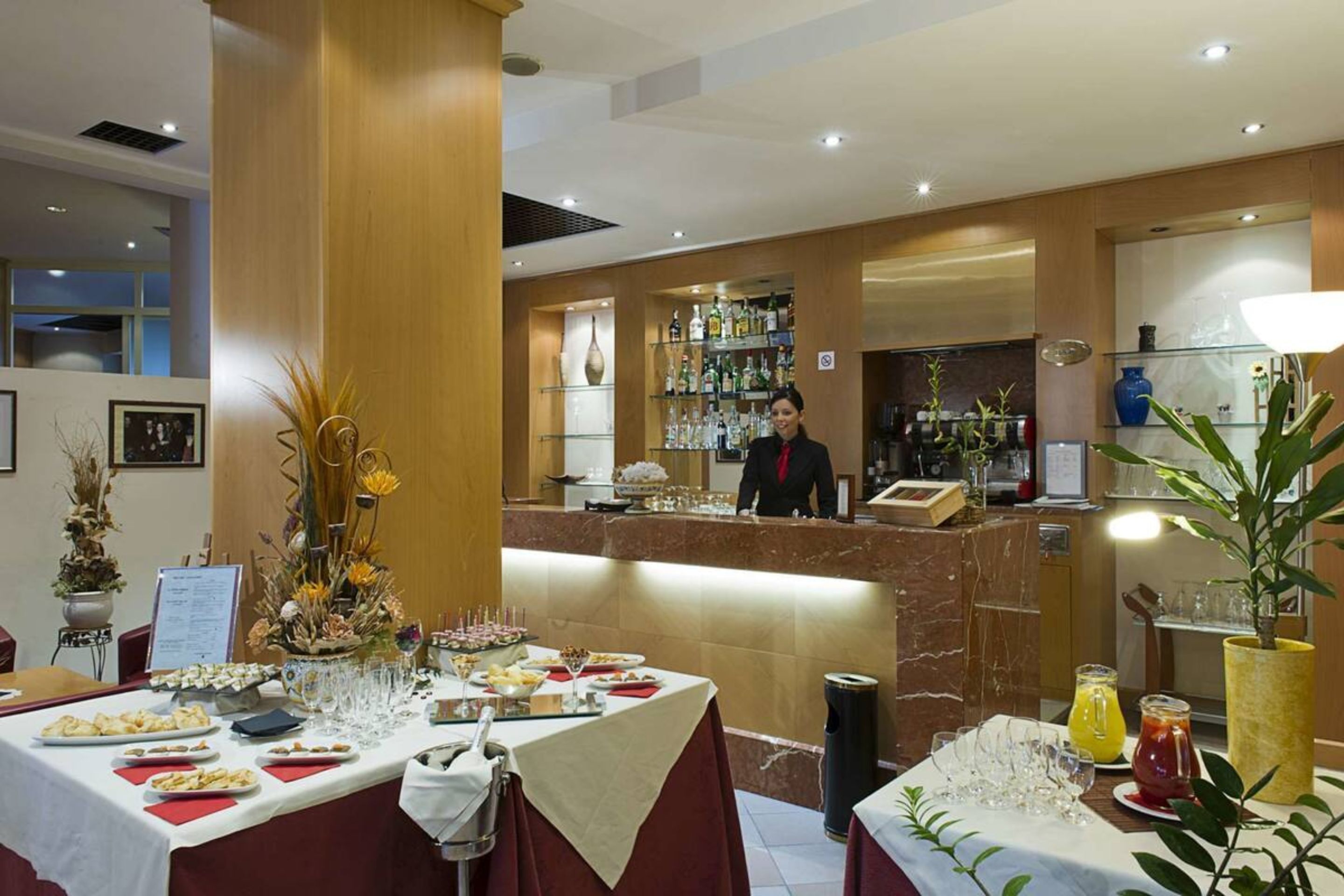 A hotel reception area with a bar, a buffet table with various dishes, and a counter with a bartender.