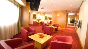 A hotel lobby with red seating, a central table with a flower arrangement, and a red carpeted floor. - Classic Hotel Tulipano (Terni)