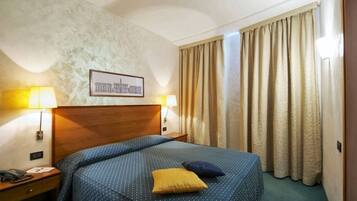 Habitación de hotel con una cama grande, dos lámparas de noche, un cuadro en la pared y una ventana con cortinas.