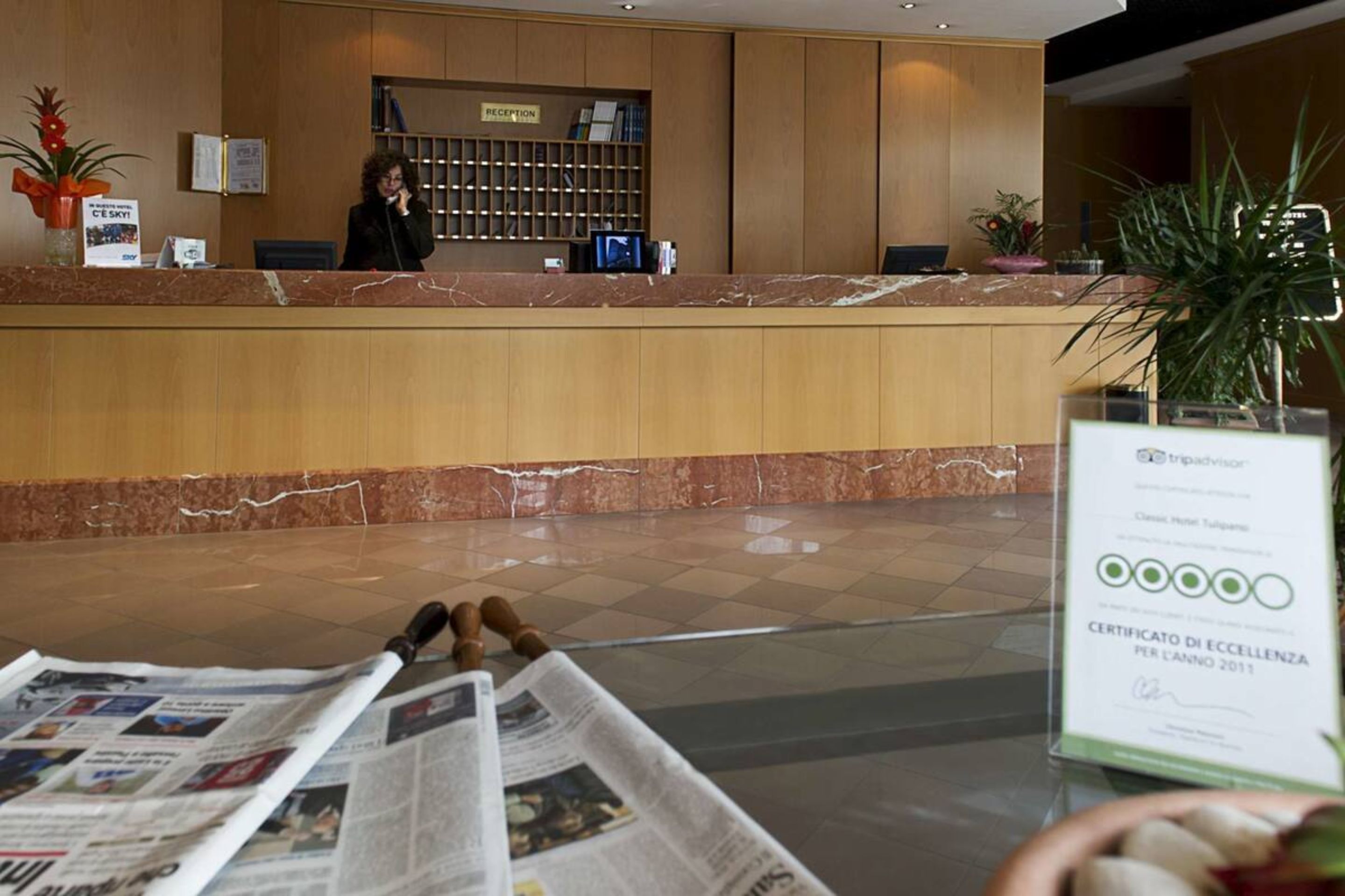 Zona de recepción de hotel con mostrador de mármol, escritorio de recepción y un cartel que indica la recepción.