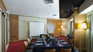 A conference room with a long table, chairs, a whiteboard, and a projector screen.